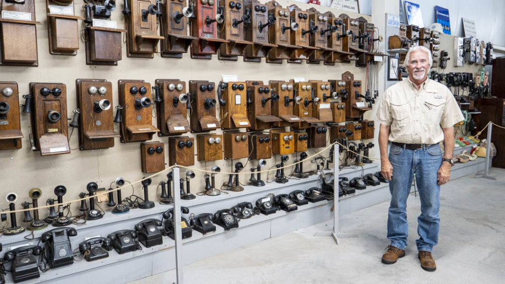 Art Peters standing in front of a collection of telephones at the Hinton Historical Museum - photo by Dennis Spielman